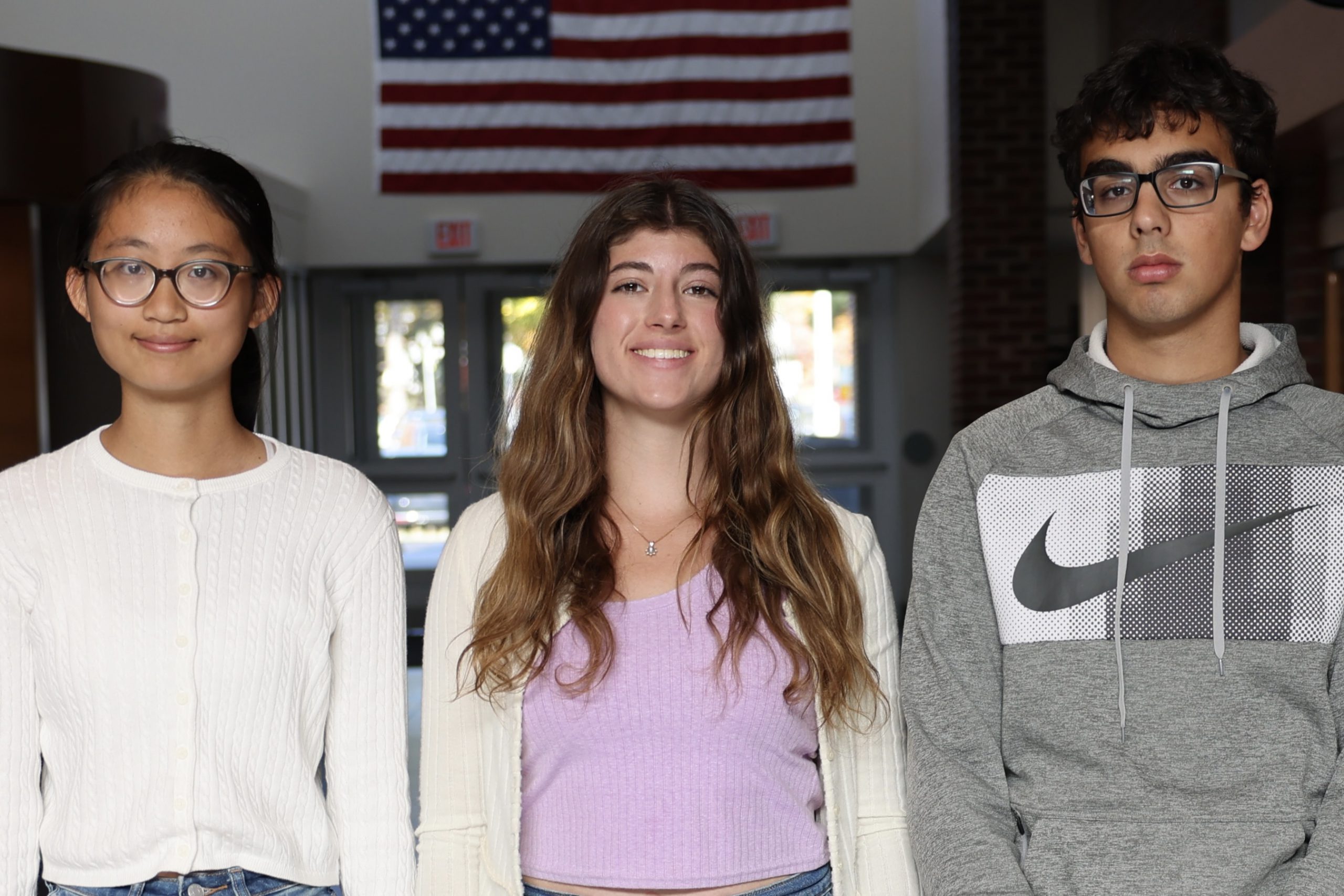 three students standing in school hallway